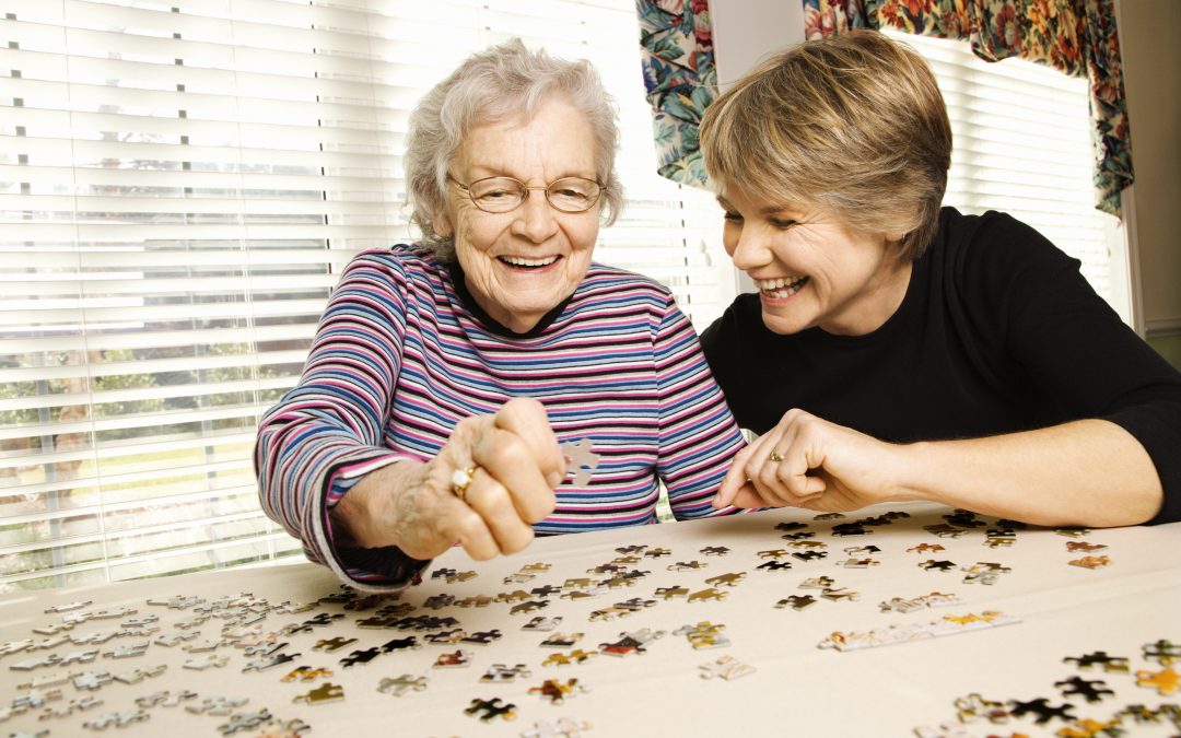 Elderly Woman and Younger Woman Doing Puzzle In Assisted Living Home